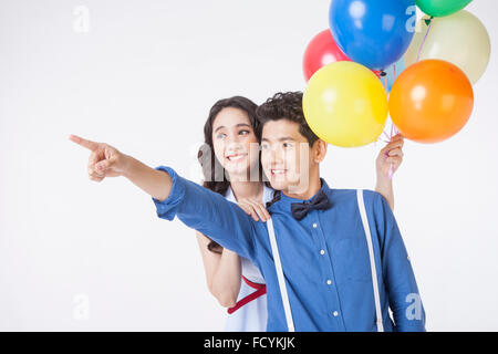 Couple en tenues décontractées avec un doigt de l'homme orientée vers le haut et avec des ballons colorés dans la main de femme à la fois smiling Banque D'Images