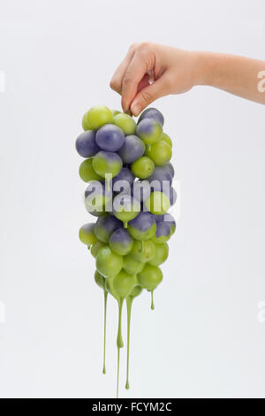 Peint peinture verte sur le raisin dégoulinant tenu par une main Banque D'Images