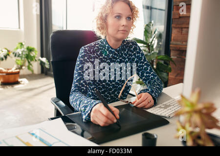 Jeune femme rédactrice à l'aide de tablette graphique pour travailler à son bureau dans le bureau. Graphiste professionnel au travail. Banque D'Images