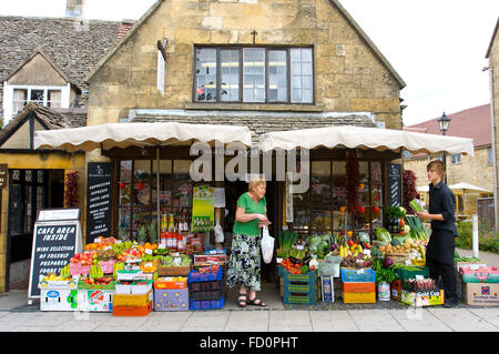 Une dame âgée et shop keeper à broadwaydeli boutique sur High Street, dans le centre du village de Broadway, Cotswolds, Royaume-Uni. Banque D'Images