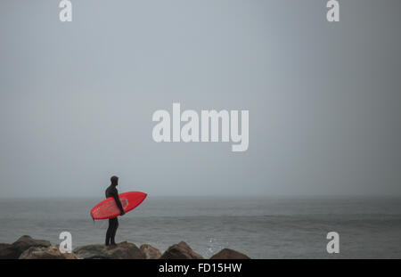 Avec surfeur surf rouge debout sur la roche jetti. Photographié à Rockaway Beach, Queens, New York le 29 décembre 2015. Banque D'Images