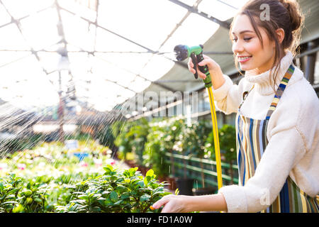 Pretty woman Happy gardener en uniforme l'arrosage des plantes avec des émissions de tuyau de jardin Banque D'Images