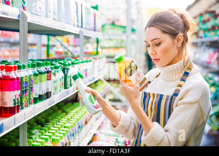 Jeune femme concentrée en choisissant des produits chimiques agricoles pour fleurs et plantes en magasin Banque D'Images