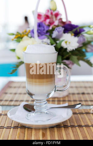 Latte dans un verre avec un arrière-plan flou d'un beau bouquet de fleurs. Soft focus sélectif. Banque D'Images