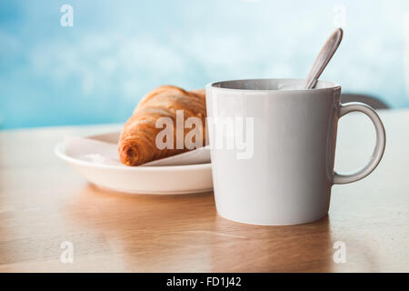 Cappuccino avec un croissant. Tasse de café avec mousse de lait se dresse sur une table en bois dans une cafétéria sur fond flou, closeu bleu Banque D'Images