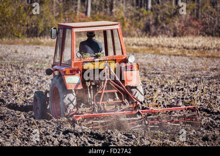 Agriculteur dans le tracteur pour préparer les terres pour les semis, de l'Agriculture et de travail. Le Labour tracteur rouge à l'automne, la préparation de plan de champ Banque D'Images