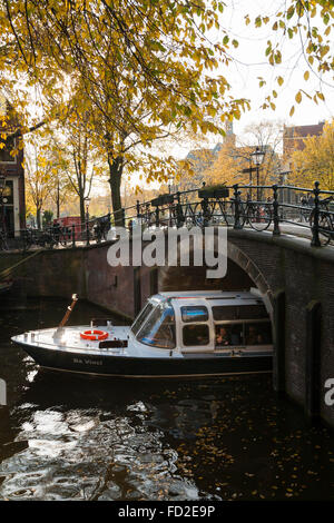 Bateau de tourisme / barge en passant sous un pont-canal Automne / fall avec sun / sunny blue sky à Amsterdam, Hollande. Les Pays-Bas Banque D'Images