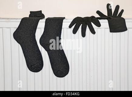 Une paire de gants noirs et des chaussettes humides sécher sur un radiateur dans une chambre. Banque D'Images