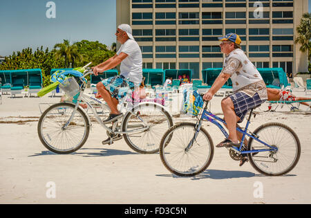 Deux hommes chargés d'engins de plage vélo le long du rivage sur leurs vélos cruiser en face de baigneurs et les condos en Floride Banque D'Images