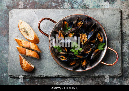 Les moules dans un plat de cuisson en cuivre et baguette française avec des herbes sur fond ardoise Banque D'Images