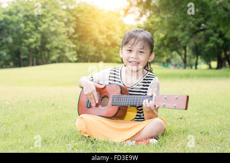 Petite fille asiatique assis sur l'herbe et jouer ukulele in park Banque D'Images