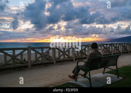 Un homme est assis sur un banc de parc avec vue sur le coucher du soleil sur l'océan. Santa Monica, Californie. Banque D'Images