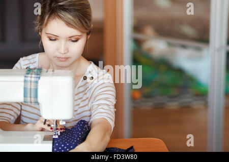 Jeune femme avec machine à coudre coudre à la maison tout en restant assis par son lieu de travail. Fashion designer créant de nouveaux styles à la mode. Couturière vêtements fait par emploi à temps partiel. Copier l'espace. Banque D'Images