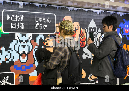Les piétons devant une immense murale Dragon Quest fait en blocs Lego Le 27 janvier 2016 à Tokyo, Japon. La fresque fait partie d'une promotion à la gare de Shinjuku pour fêter la sortie de nouveau le jeu Dragon Quest les constructeurs. La murale a été faite de 80 mètres avec 180 000 les blocs de Lego et les fans seront autorisés à supprimer des blocs à partir du 28 janvier pour révéler un secret derrière l'affiche. Certains blocs contiennent aussi des codes QR permettant aux fans d'accéder à des contenus exclusifs. © Rodrigo Reyes Marin/AFLO/Alamy Live News Banque D'Images