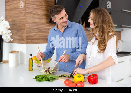 Heureux couple couper des légumes et à faire sur l'ensemble de cuisine salade Banque D'Images