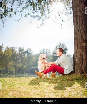 Cheerful man par un arbre dans le parc et jouer avec son chien de compagnie shot Objectif de décentrement et de Banque D'Images