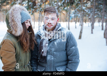 Beau jeune homme barbu avec de la neige sur son visage et gai jolie jeune femme debout et riait dans winter park Banque D'Images