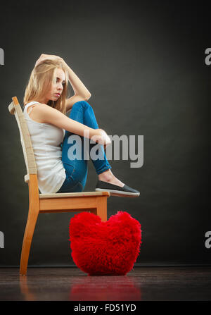 Broken Heart Love concept. Triste Malheureux woman sitting on chair coeur rouge sur fond sombre plancher Banque D'Images