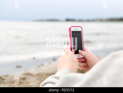 Femme prenant une photo de l'océan avec son smartphone moderne blanc et rose modèle libération : Oui. Biens : Non. Banque D'Images