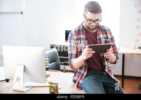 Portrait de jeune homme barbu assis avec tablette sur la table in office Banque D'Images