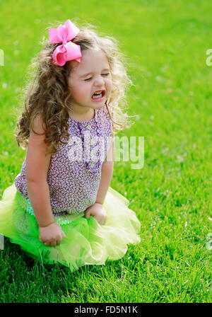 Bébé fille à genoux dans l'herbe avec une très frustré expression sur son visage. Banque D'Images