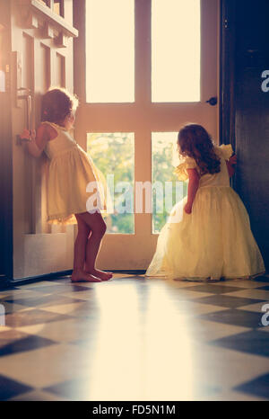 Deux petites filles en robes jaunes fixant leur porte avant que le soleil de l'après-midi en poutres apparentes. Banque D'Images