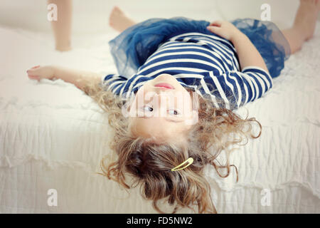 Image d'une petite fille portant sur son lit avec sa tête accroché à l'extérieur du bord de sorte qu'elle est à l'envers. Banque D'Images