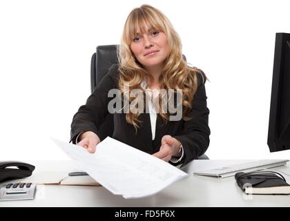 Smiling attractive young blond businesswoman handing over un document qui s'étend sur son bureau avec les papiers dans sa main Banque D'Images