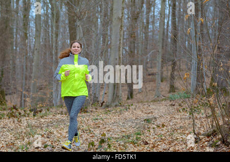 Young woman jogging à travers bois d'hiver haute visibilité portant un top pour la sécurité qu'elle aime son entraînement quotidien dans un Banque D'Images