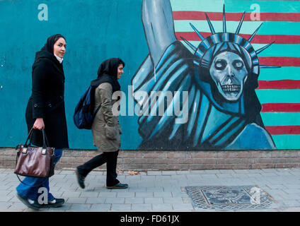 Les femmes en passant en face de propagande murale anti-américaine dépeignent slogan statue liberty skeleton sur le mur de l'ancienne ambassade des États-Unis, Central District, Téhéran, Iran Banque D'Images