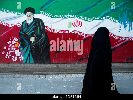 Femme voilée en passant en face de la propagande signe avec l'ayatollah Khomeiny sur le mur de l'ancienne ambassade des États-Unis, Central District, Téhéran, Iran Banque D'Images