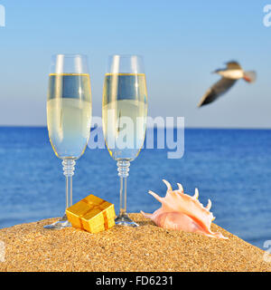 Verres de champagne, fort avec un cadeau et un coquillage sur la plage contre le ciel et mer bleue Banque D'Images