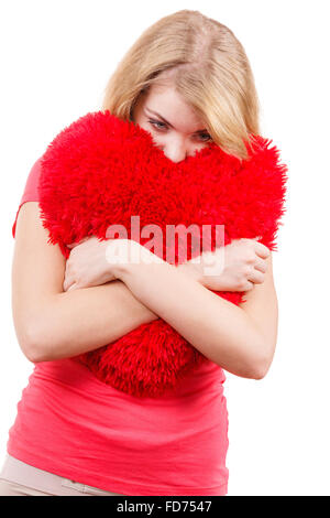 Femme blonde triste malheureux girl hugging grand coussin en forme de coeur rouge, studio shot on white. Navré de jeunes femelles. Banque D'Images