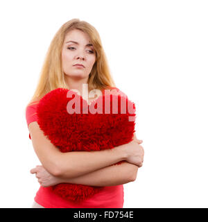 Femme blonde triste malheureux girl hugging grand coussin en forme de coeur rouge, studio shot on white. Navré de jeunes femelles. Banque D'Images