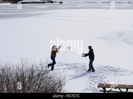 Les jeunes jouant sur un lac gelé de jeter un grand bal de neige. Banque D'Images