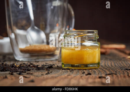 Verre de miel jaune en face d'un teaglass avec du sucre brun sur la vieille table en bois Banque D'Images