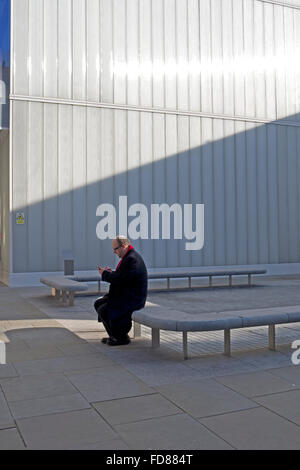 Un homme est assis sur le siège de béton au texte en plein milieu urbain. Banque D'Images