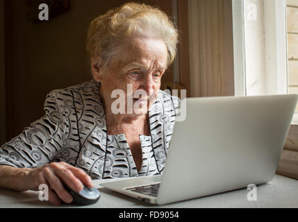 Une femme âgée assise à la table et les types sur ordinateur portable. Banque D'Images