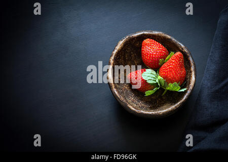 Fraises fraîches dans Bol en céramique marron sur fond noir. Le tableau Vue de dessus, Copy Space Banque D'Images