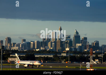 Jetstar aéronefs atterrissant sur l'aéroport Kingsford-Smith, tour de la CDB dans les bâtiments distnace, Sydney, New South Wales, Australia Banque D'Images