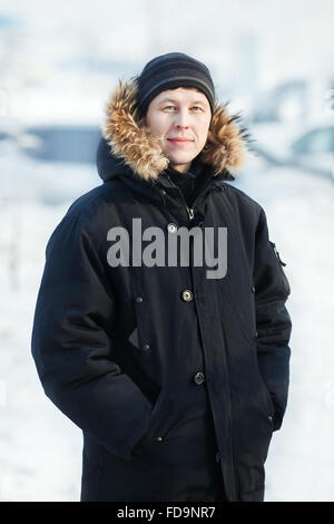 Portrait d'un jeune homme de Sibérie en hiver froid jour, porter au chaud Down jacket with fur Hood, à la verticale. La neige, le gel. En regardant la caméra. Banque D'Images