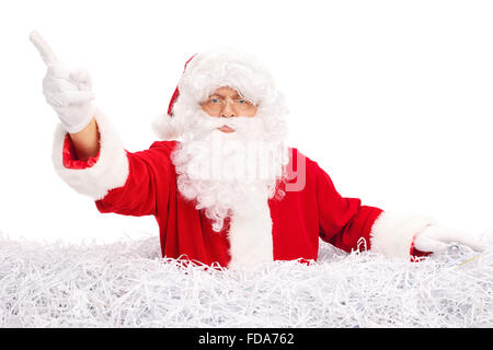 Père Noël en colère pointant avec son doigt et se tenant dans une pile de papier déchiqueté isolé sur fond blanc Banque D'Images