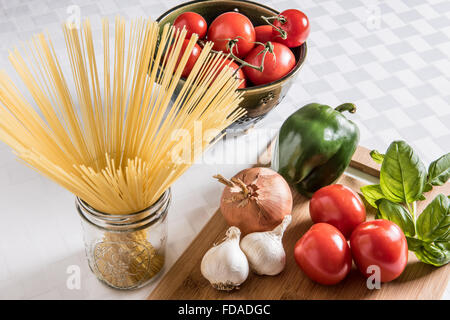 Des ingrédients frais italiens sont exposés sur une planche à découper en bois avec des pâtes à cheveux d'ange séchées et une passoire en céramique de tomates mûres sur un chiffon blanc. Banque D'Images