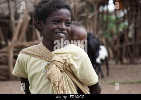 Une jeune Éthiopienne porte son jeune frère sur son dos dans un petit village de l'Éthiopie dans le bassin Gelana. Banque D'Images