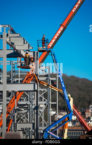 Les hommes travaillent en hauteur de 'grue' plates-formes élevées - construire ensemble le cadre en acier de boulonnage d'un nouveau bâtiment qui abritera une succursale de supermarché Tesco et Marks & Spencer store, sur un ciel bleu clair jour, Aberystwyth Wales UK Banque D'Images