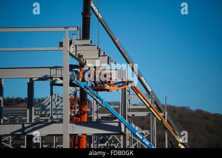 Les hommes travaillent en hauteur de 'grue' plates-formes élevées - construire ensemble le cadre en acier de boulonnage d'un nouveau bâtiment qui abritera une succursale de supermarché Tesco et Marks & Spencer store, sur un ciel bleu clair jour, Aberystwyth Wales UK Banque D'Images