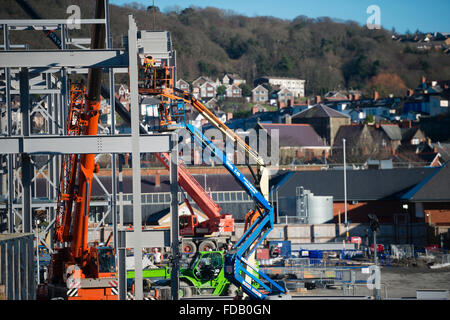 Les hommes travaillent en hauteur de 'grue' plates-formes élevées - construire ensemble le cadre en acier de boulonnage d'un nouveau bâtiment qui abritera une succursale de supermarché Tesco et Marks & Spencer store, sur un ciel bleu clair jour, Aberystwyth Wales UK Banque D'Images