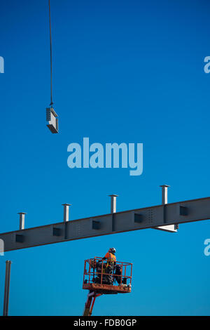 Les hommes travaillent en hauteur de 'grue' plates-formes élevées - construire ensemble le cadre en acier de boulonnage d'un nouveau bâtiment qui abritera une succursale de supermarché Tesco et Marks & Spencer store, sur un ciel bleu clair jour, Aberystwyth Wales UK Banque D'Images