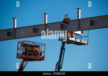 Les hommes travaillent en hauteur de 'grue' plates-formes élevées - construire ensemble le cadre en acier de boulonnage d'un nouveau bâtiment qui abritera une succursale de supermarché Tesco et Marks & Spencer store, sur un ciel bleu clair jour, Aberystwyth Wales UK Banque D'Images