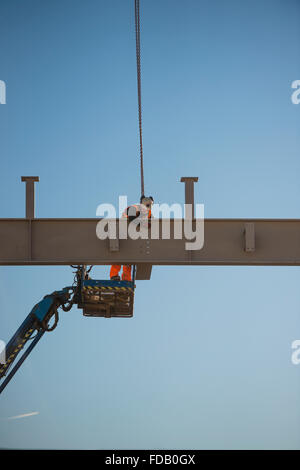 Les hommes travaillent en hauteur de 'grue' plates-formes élevées - construire ensemble le cadre en acier de boulonnage d'un nouveau bâtiment qui abritera une succursale de supermarché Tesco et Marks & Spencer store, sur un ciel bleu clair jour, Aberystwyth Wales UK Banque D'Images